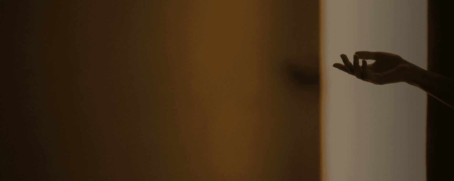 Close-up of a hand reaching toward a shoulder in soft, warm light